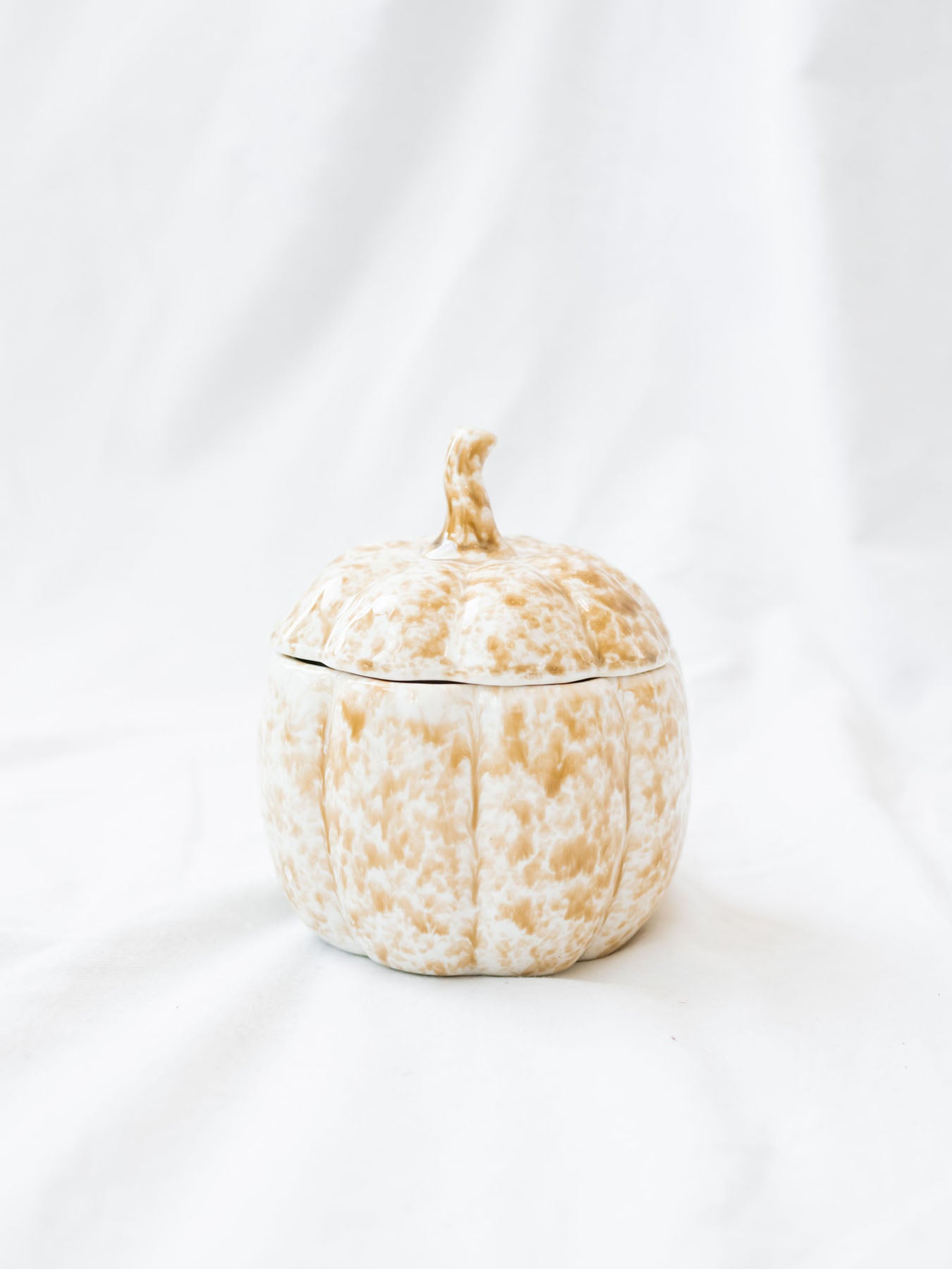 Stoneware pumpkin shaped jar with lid on top sitting on white linen backdrop.