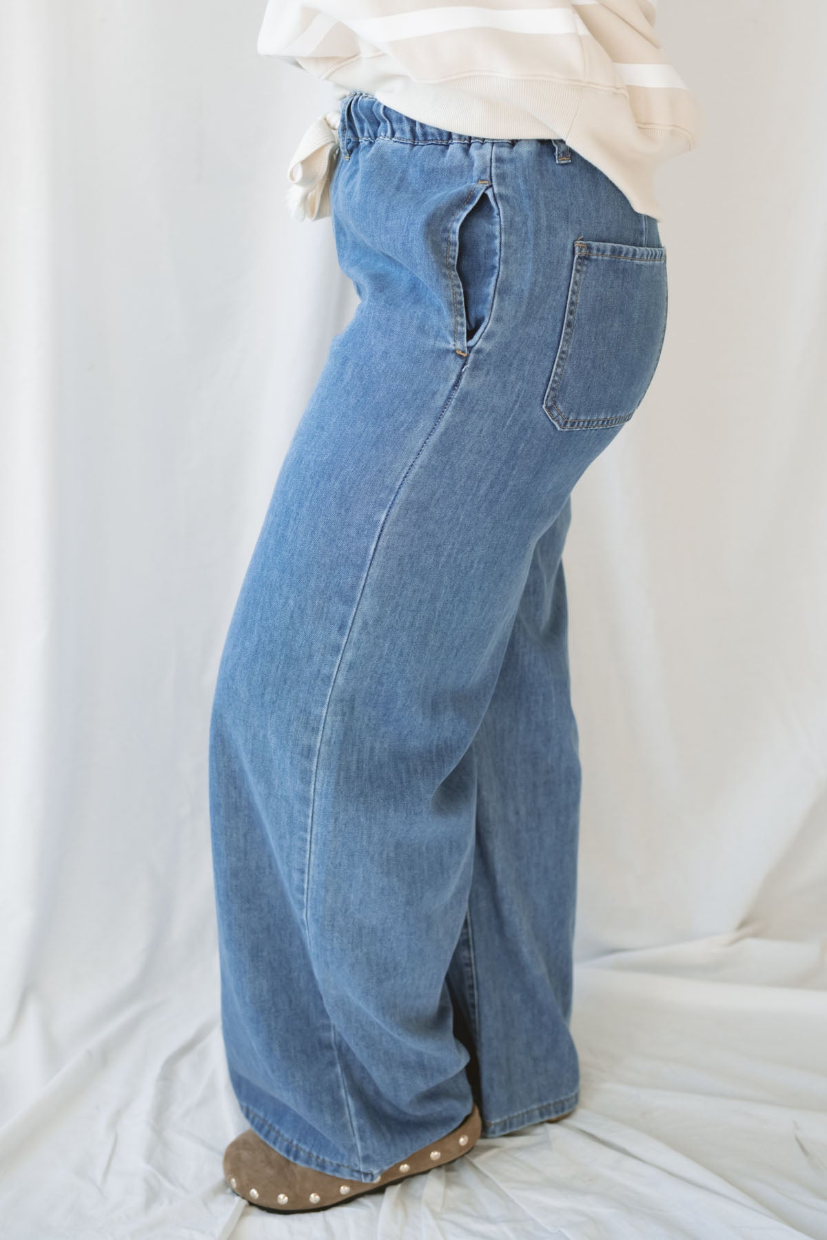 Woman wearing wide leg medium wash denim with drawstring waistband with taupe sweatshirt on a white background.