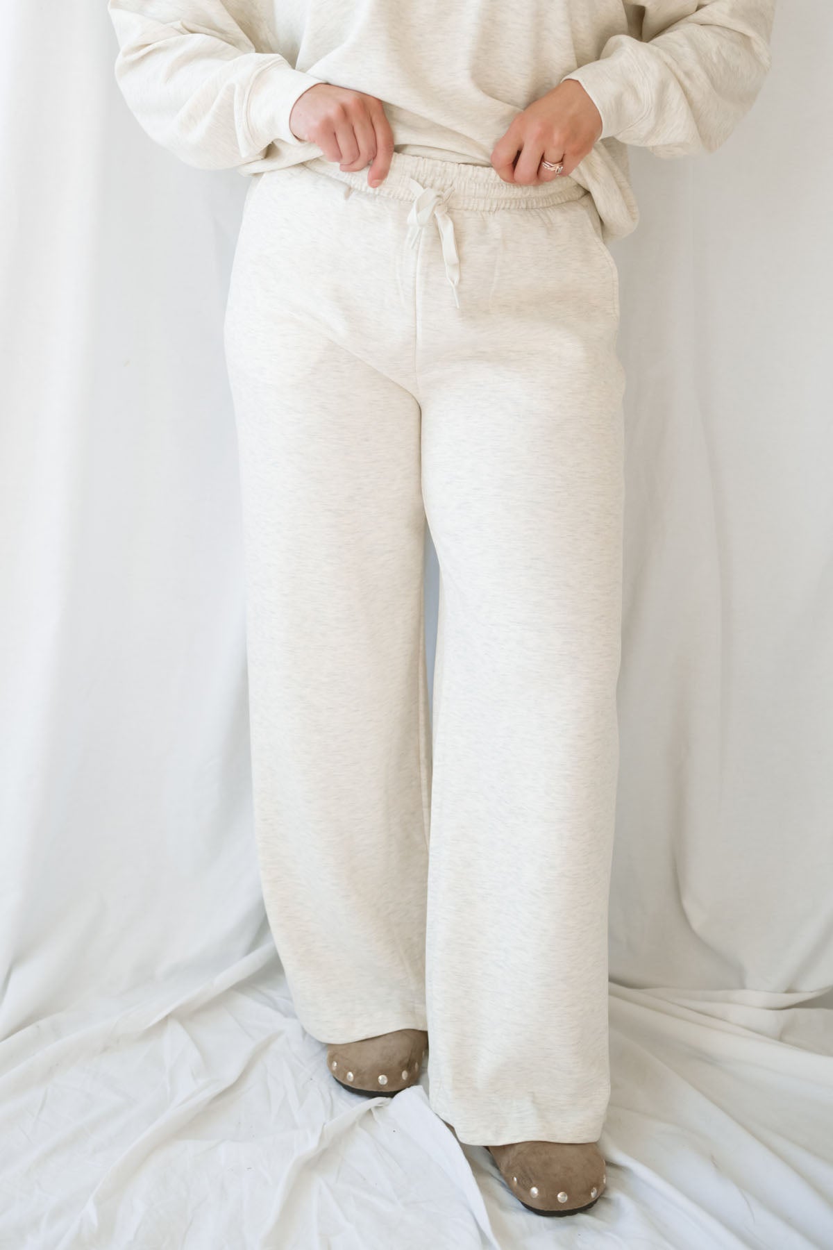 Woman wearing a light beige lounge set with crew neck sweatshirt and drawstring pants on a white background