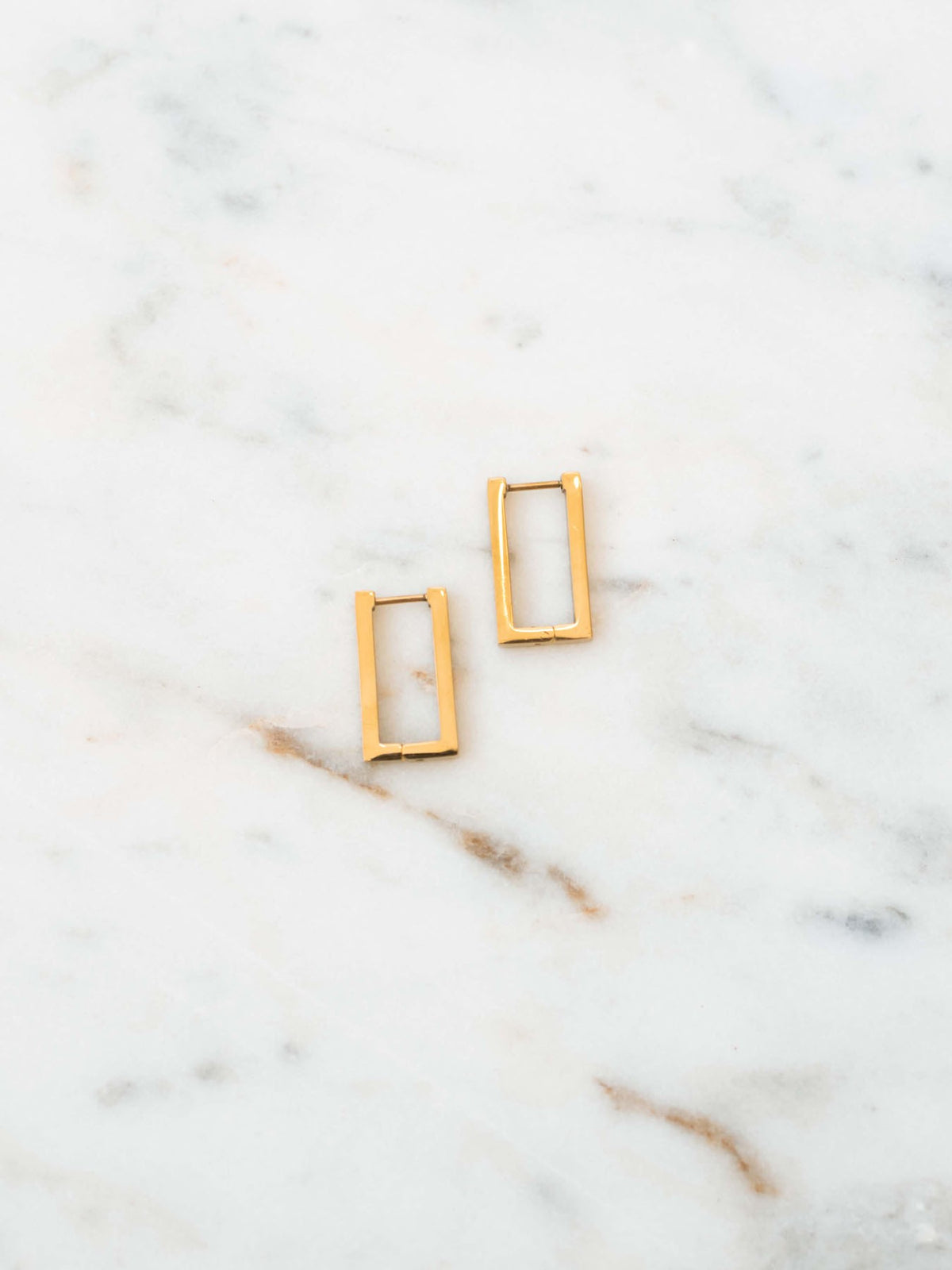 Rectangle hoop earring with stud post in gold laying on white marble board.