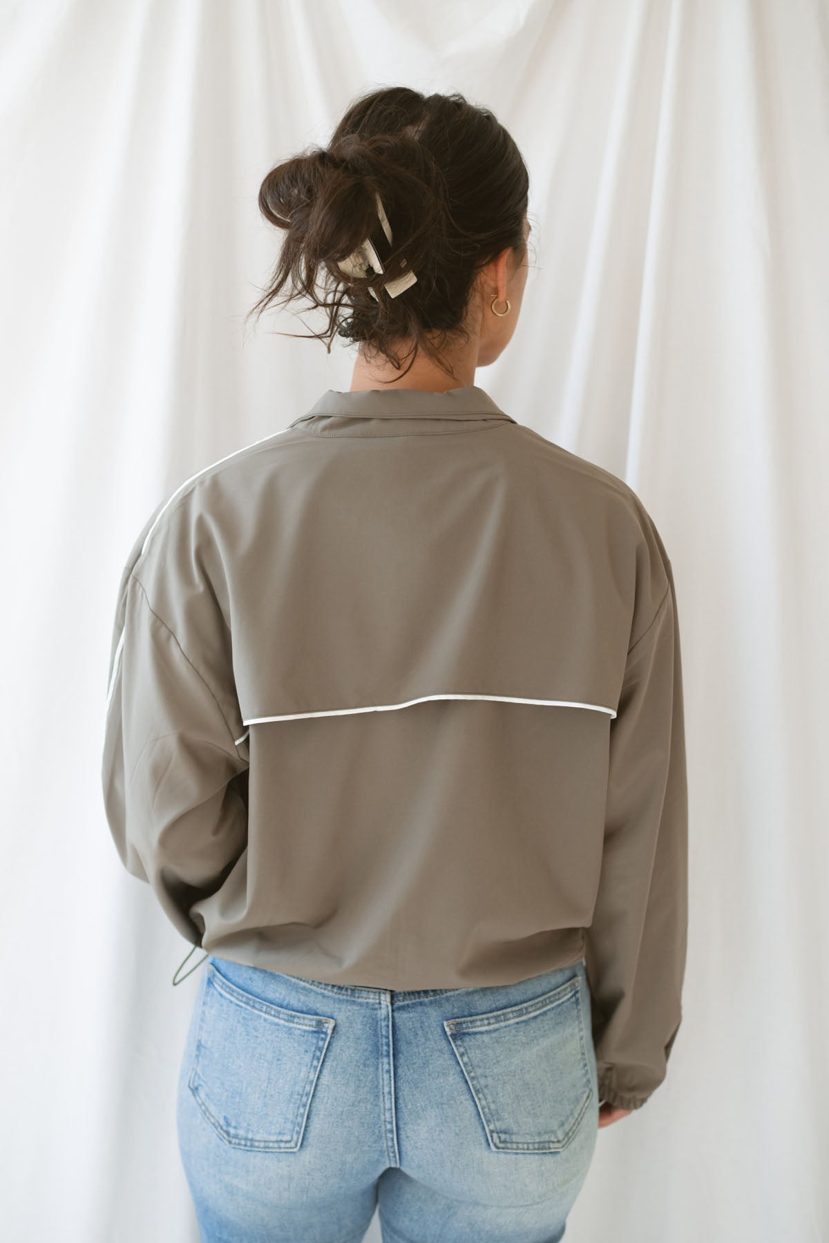 Women with dark hair wearing the truffle active jack with full zip front and pipping detail on the sleeve wearing jeans and standing in front of a white background.