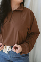 Woman wearing the half zip active jacket in cocoa with medium wash denim and standing in front of a white background 