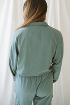 Woman with light brown hair wearing a eucalyptus half zip active jacket with collar wearing matching pants on a white background 