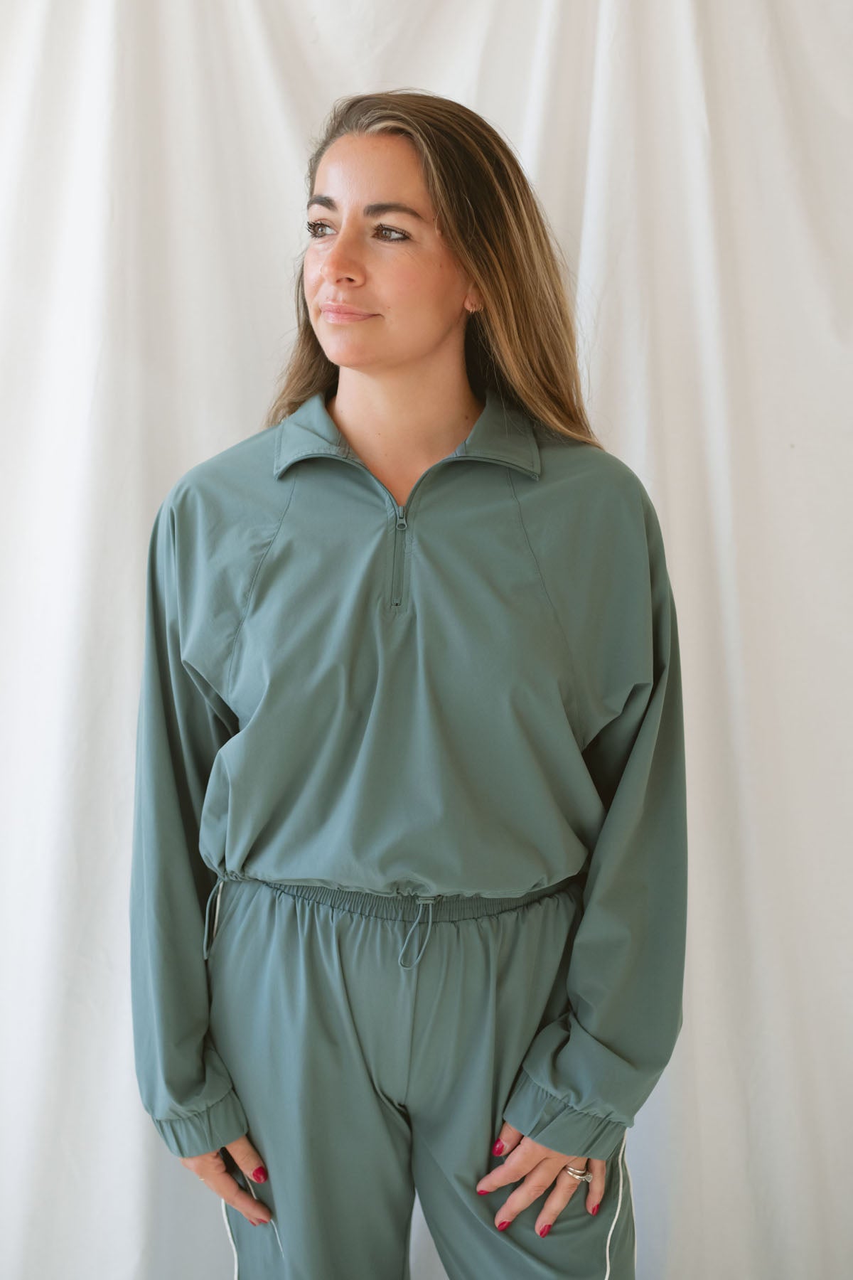 Women with light brown hair wearing a eucalyptus half zip active jacket with collar wearing matching pants on a white background 