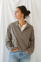Women with dark hair wearing the truffle active jack with full zip front and pipping detail on the sleeve wearing jeans and standing in front of a white background.
