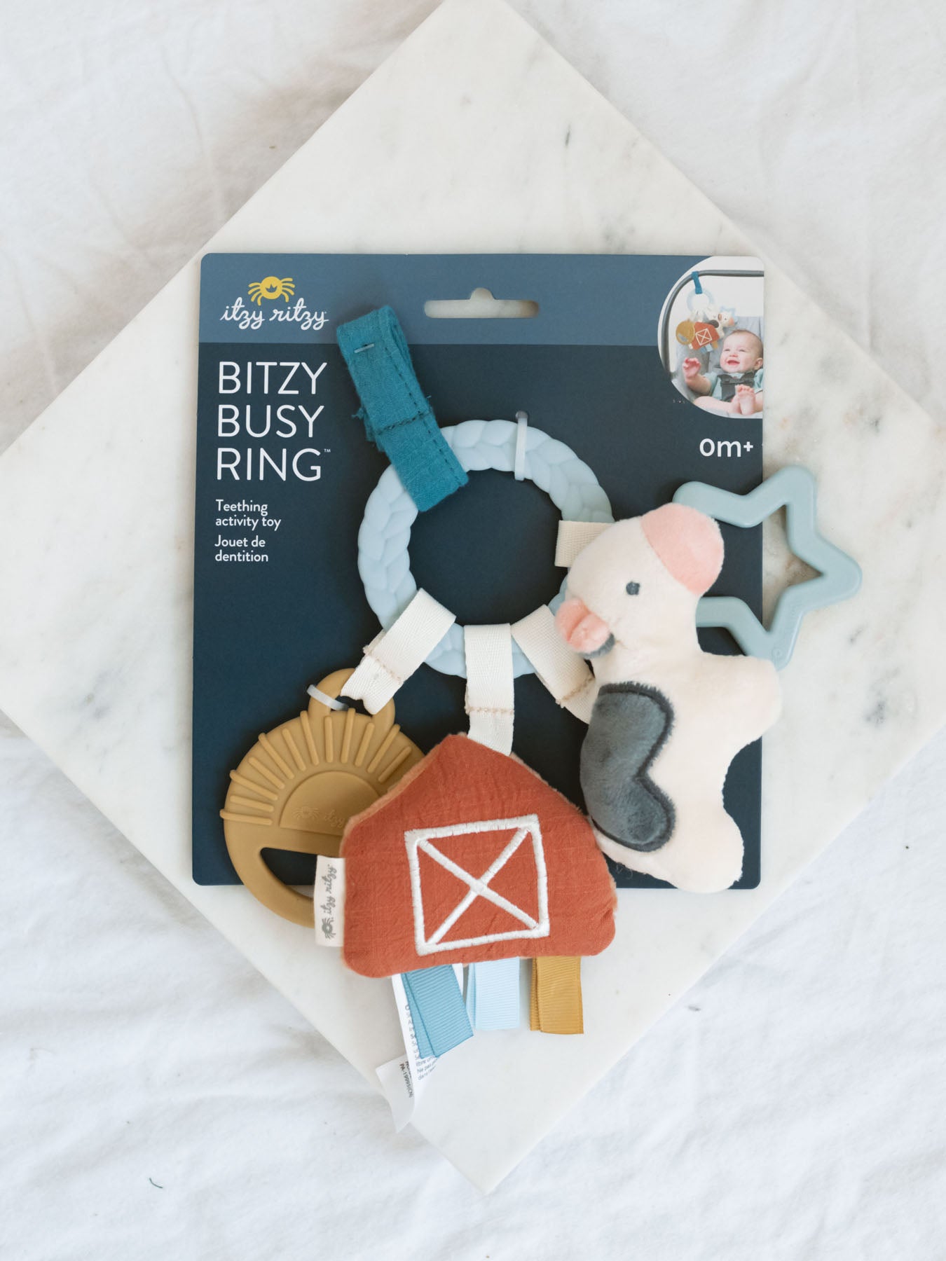 Teething activity rings with plush cow and barn. Also has a silicone sun and silicone star. Laying on a marble tray with white background 
