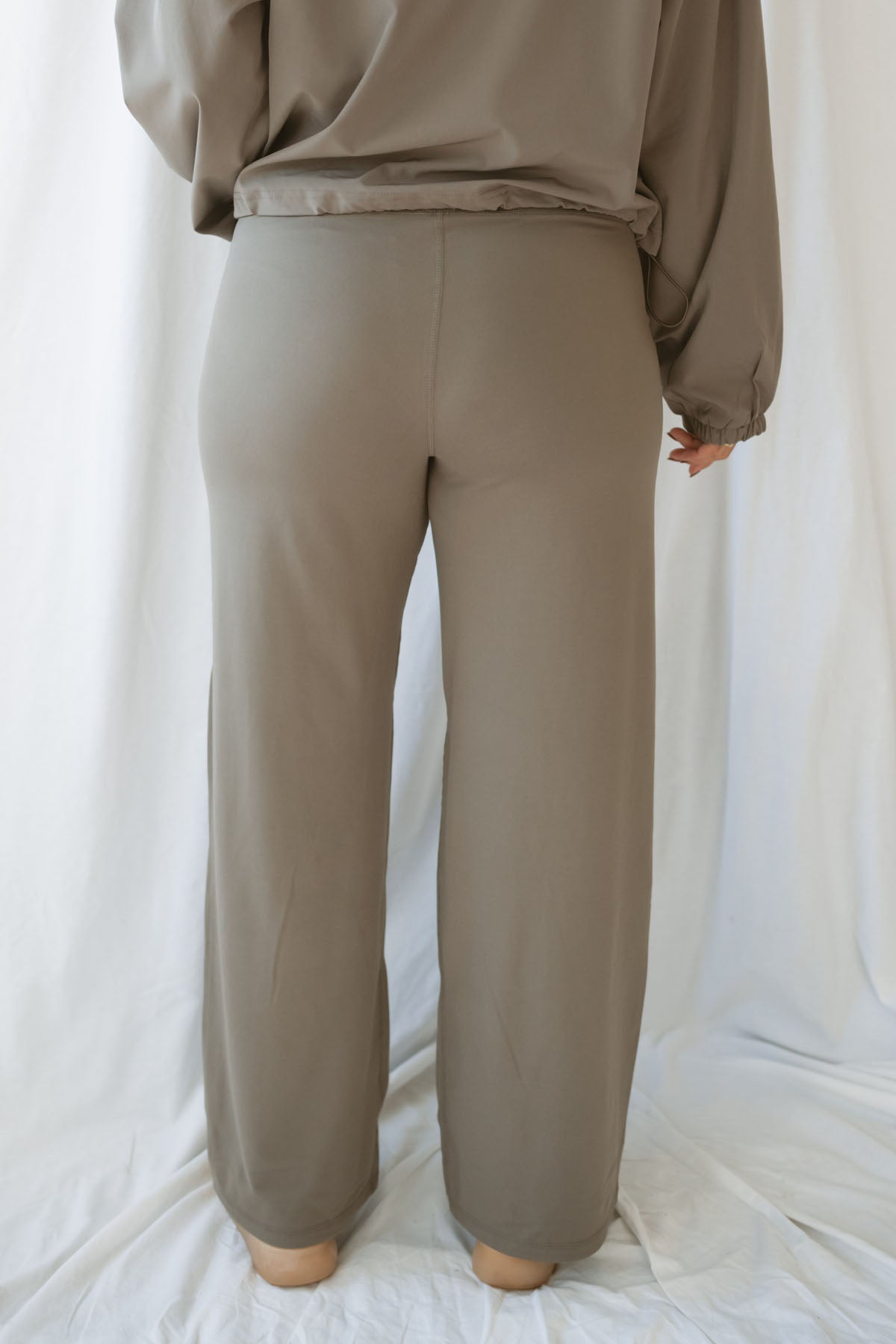 Back photo Woman wearing truffle high-waisted wide-leg pants with deep side pockets and a matching cropped jacket.