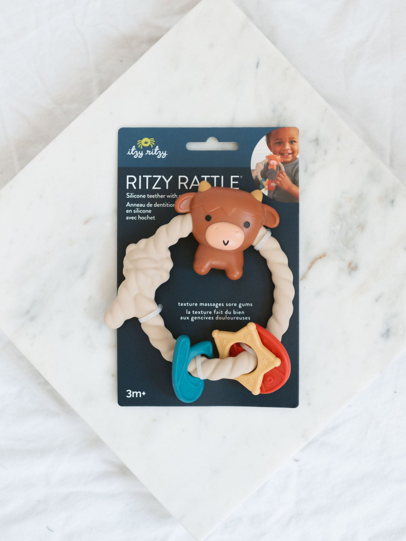 Teething ring with brown highland cow and other charms laying on a marble tray with white background