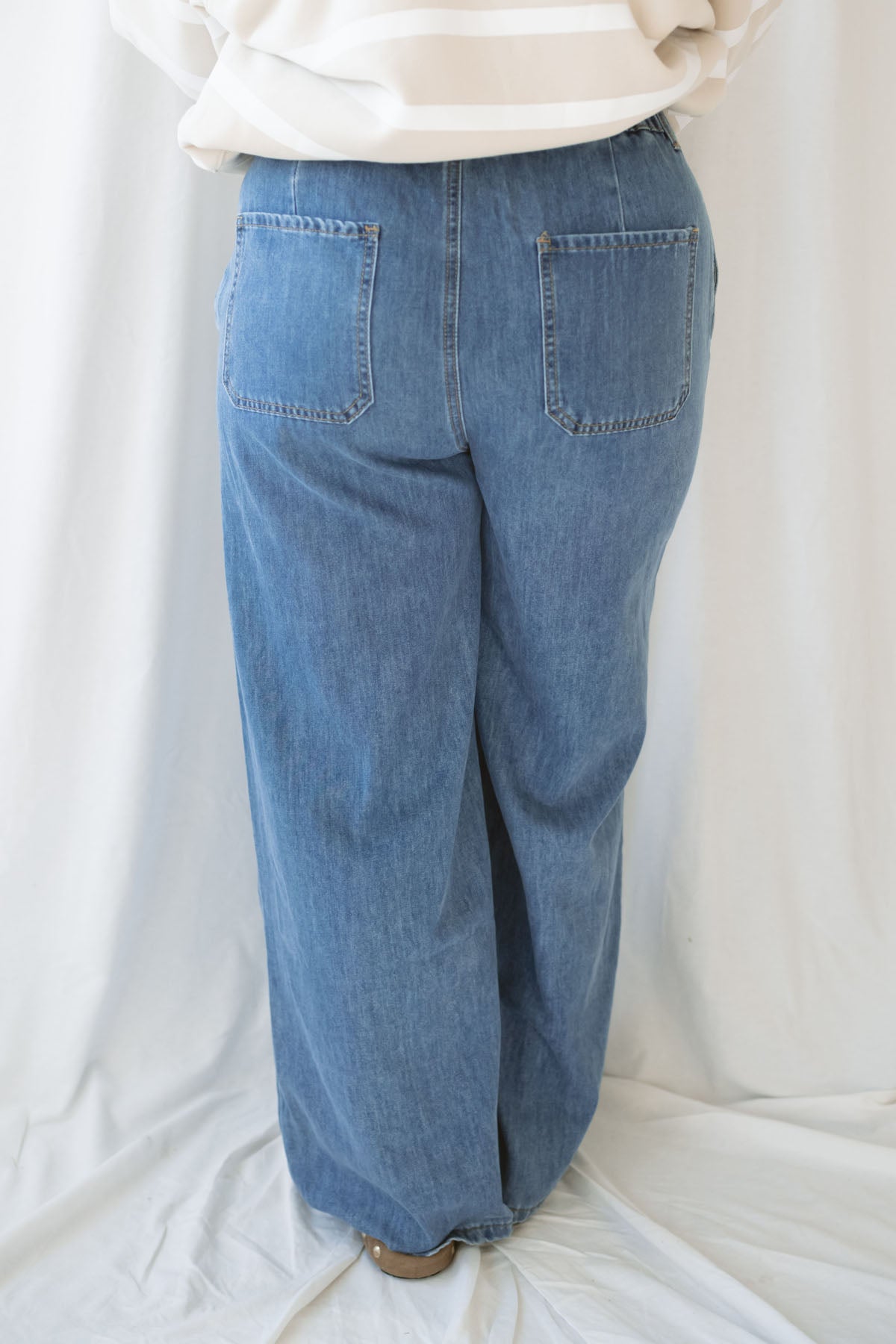 Woman wearing wide leg medium wash denim with drawstring waistband with taupe sweatshirt on a white background.
