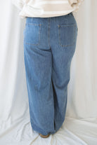 Woman wearing wide leg medium wash denim with drawstring waistband with taupe sweatshirt on a white background.