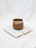 Pewter and walnut detailed wax warmer on a marble riser in front of a white background