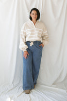 Woman wearing wide leg medium wash denim with drawstring waistband with taupe sweatshirt on a white background.