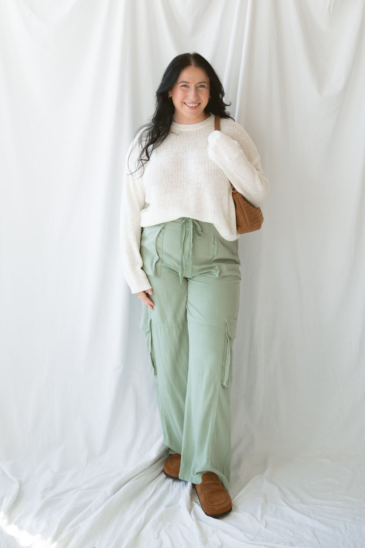 Woman wearing sage green relaxed wide-leg utility pants with oversized cargo pockets and an adjustable drawstring waist.