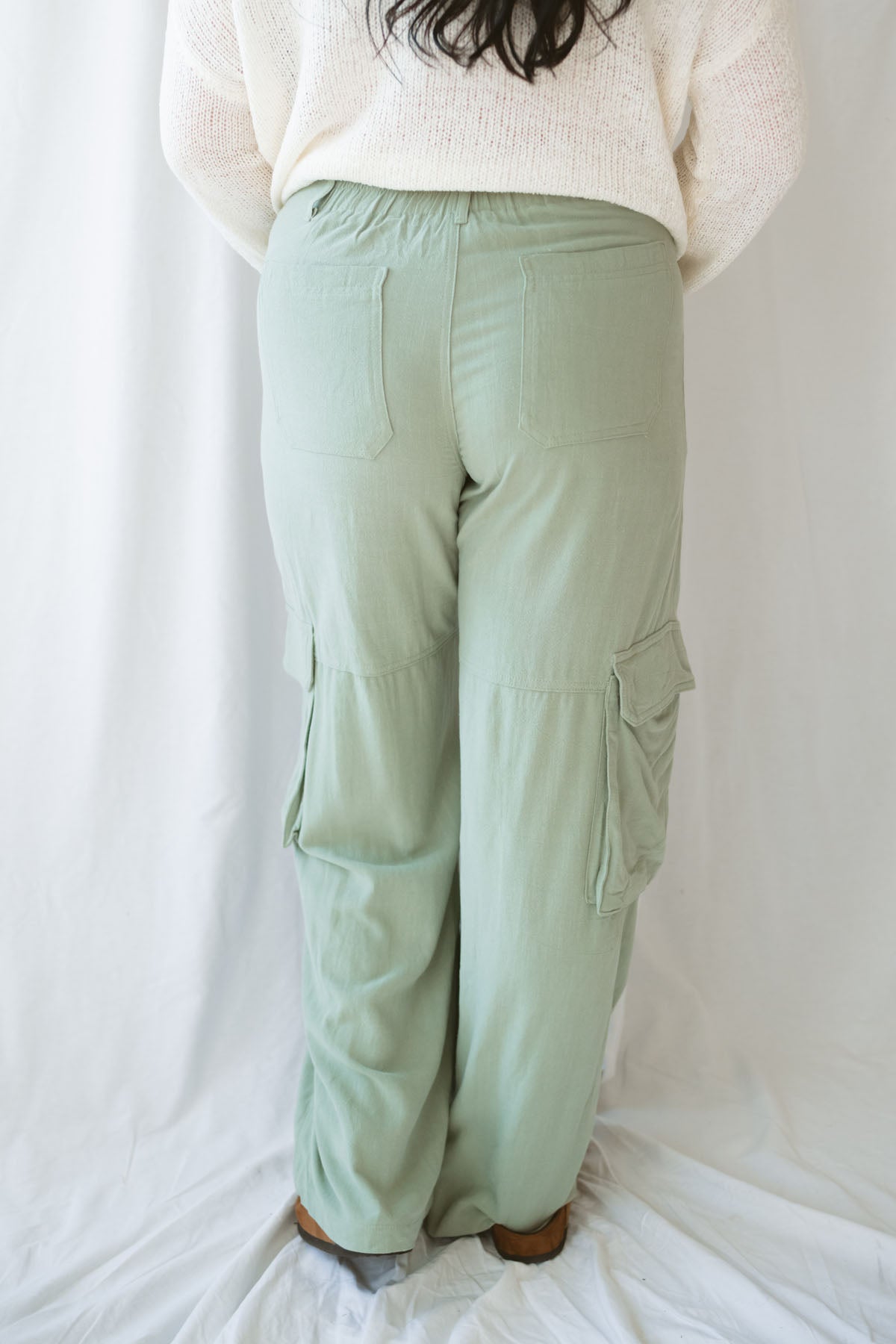 Woman wearing sage green relaxed wide-leg utility pants with oversized cargo pockets and an adjustable drawstring waist.