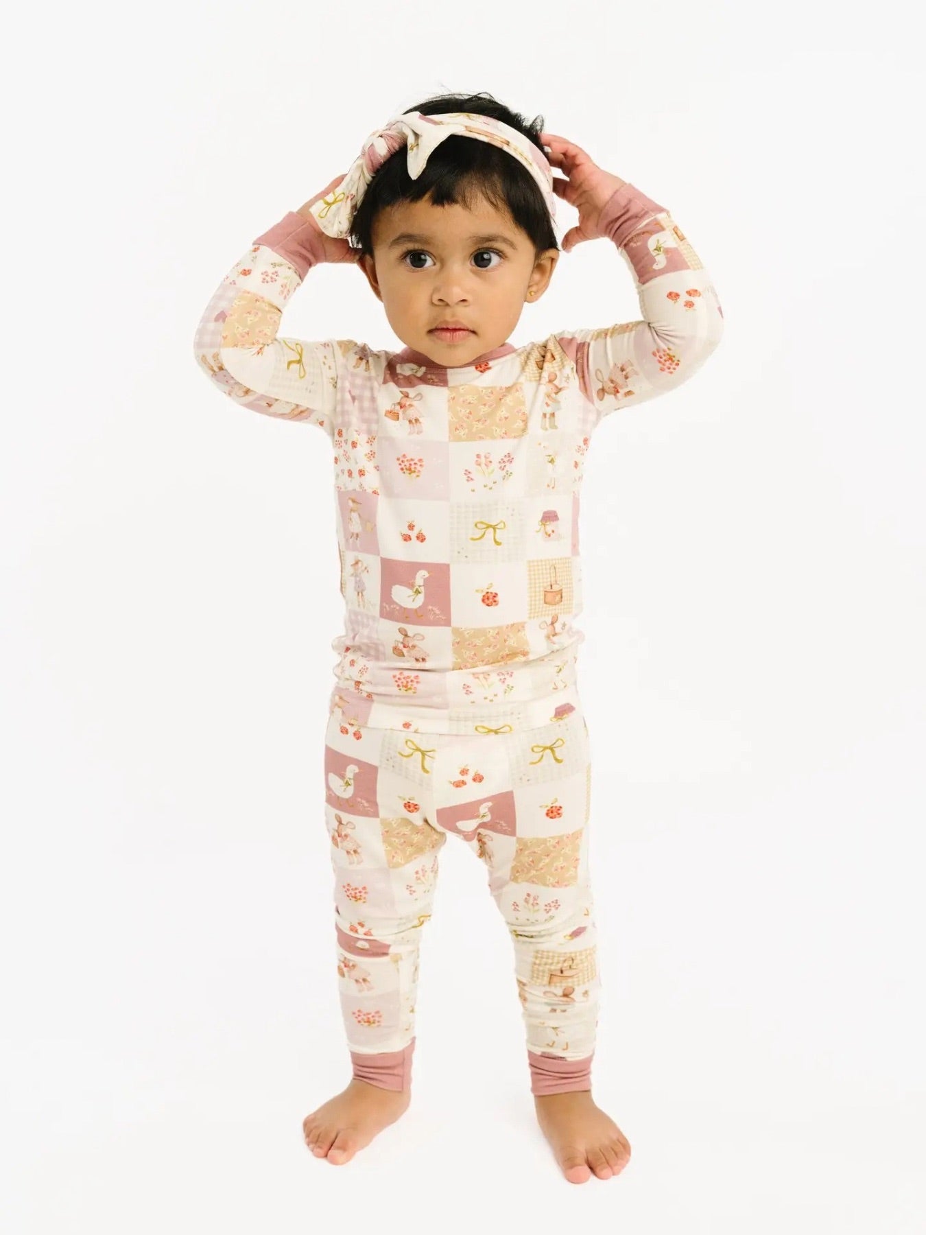 Little girl wearing a bamboo pajama top and bottom that is a quilt detail with patchwork detail of a goose, mouse, autumn floral and pink detail. 