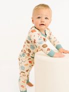 Toddler wearing a  two-piece pajama set covered in playful football icons — helmets, pretzels, foam fingers, and more — paired with dusty blue trim at the collar and cuffs on a white background 