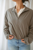 Women with dark hair wearing the truffle active jack with full zip front and pipping detail on the sleeve wearing jeans and standing in front of a white background.
