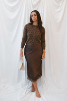 Model wearing a brown satin skirt with lace trim. Paired with a brown polka dot button up cardigan. 
