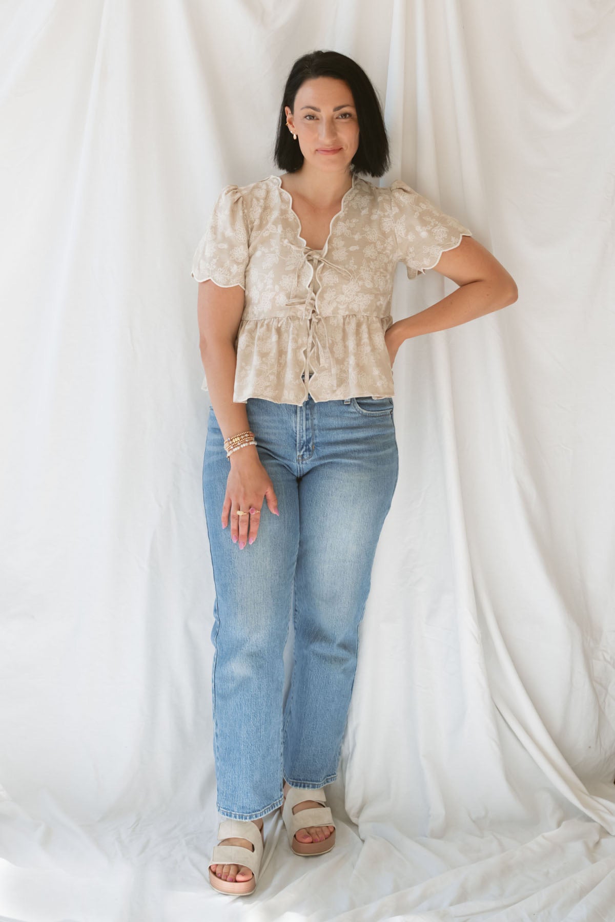 Model wearing the Floral Embroidered Front Tie Scalloped Peplum Top. Sweet and classy, this top can be dressed up easily or kept casual depending what you pair with it. 