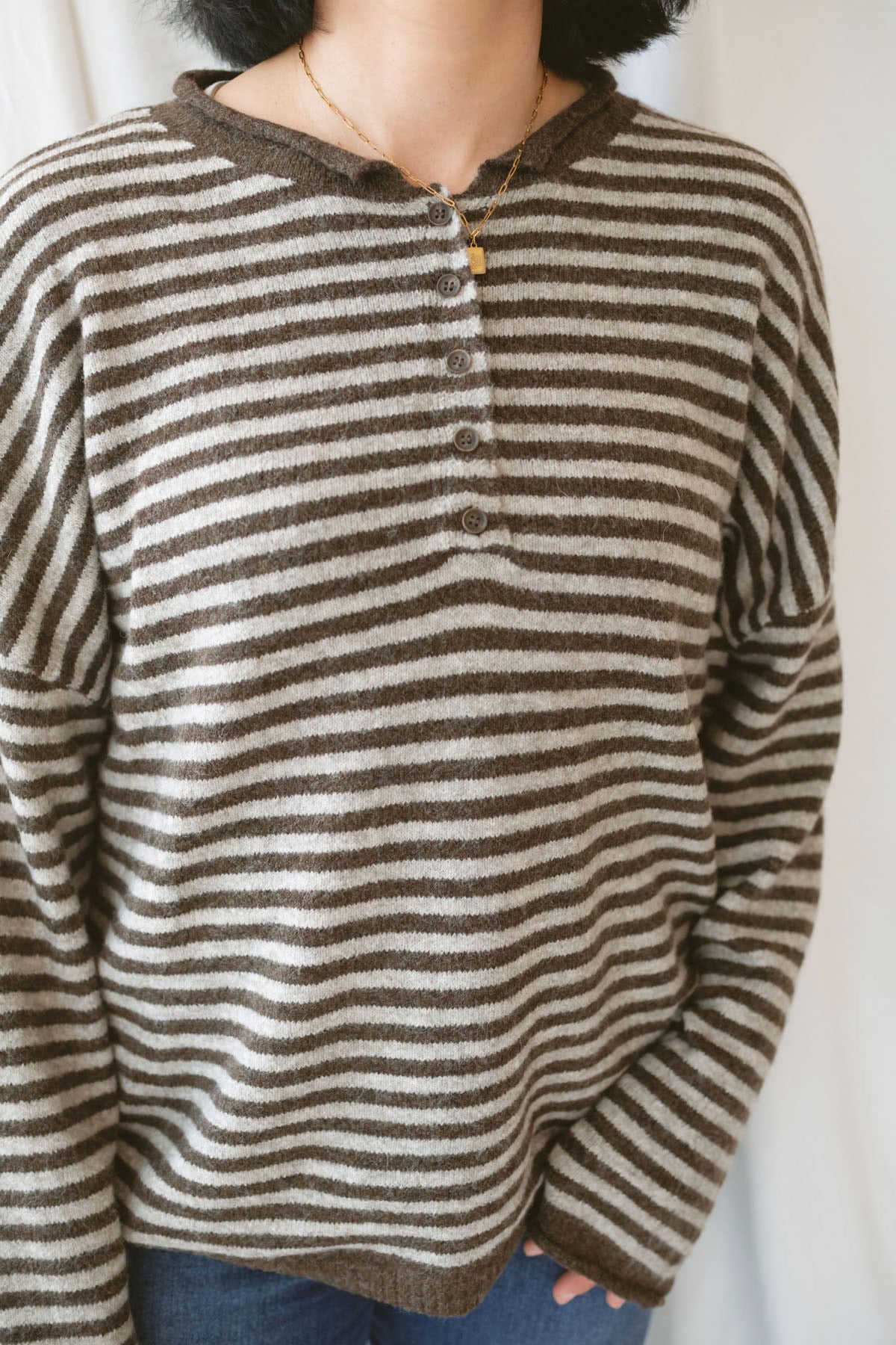 Model wearing a deep brown and tan henley button sweater. 