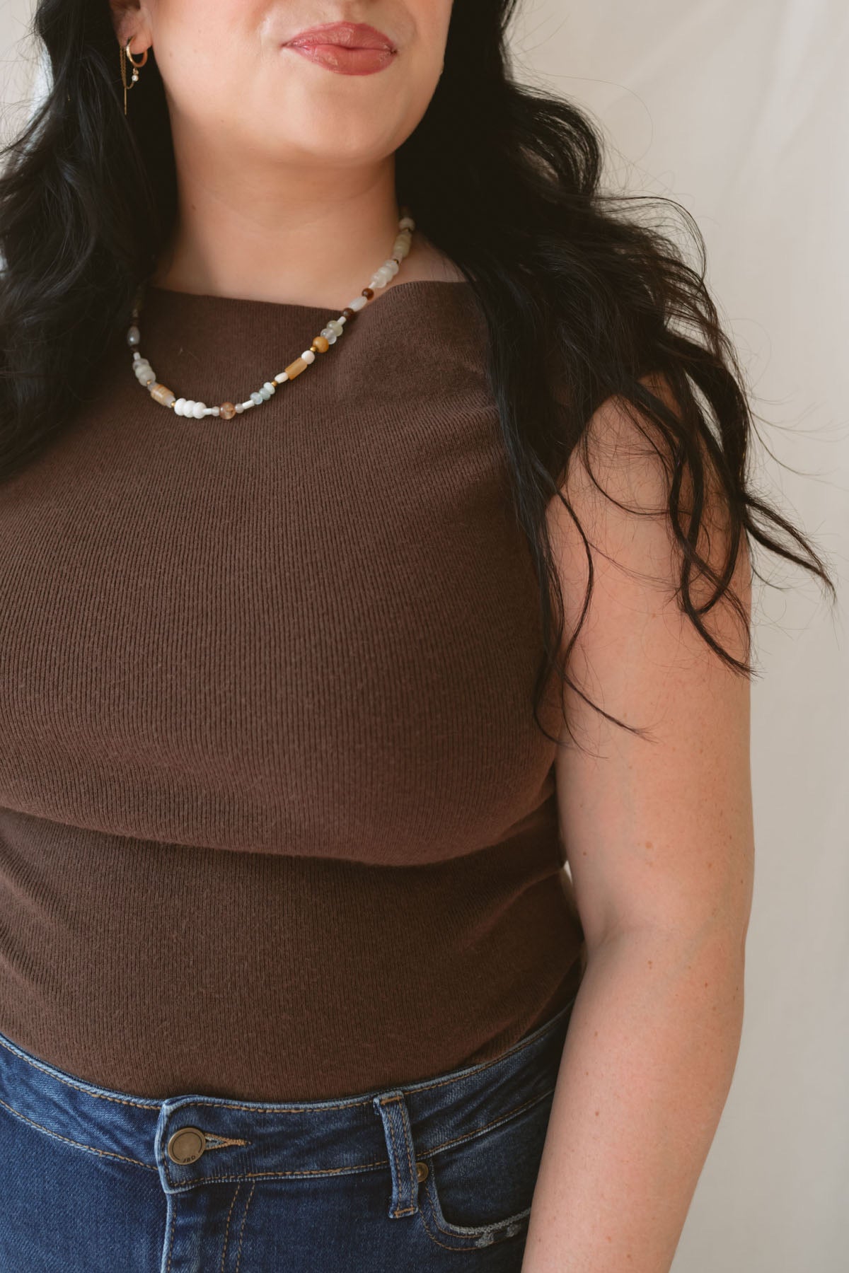 Model wearing the asymmetrical knit sweater sleeveless top with a dark pair of denim for a late summer early fall transition outfit. 
