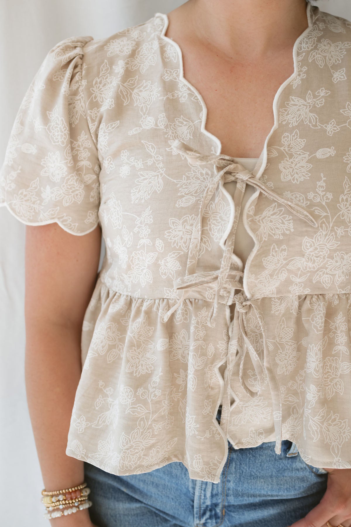 Close up of Model wearing Floral Embroidered Front Tie Scalloped Peplum Top. This top can easily be worn for special occasions or kept more casual. 