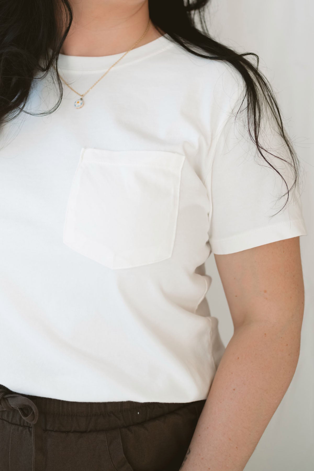 Model wearing basic white crew neck tee with pocket detail. 
