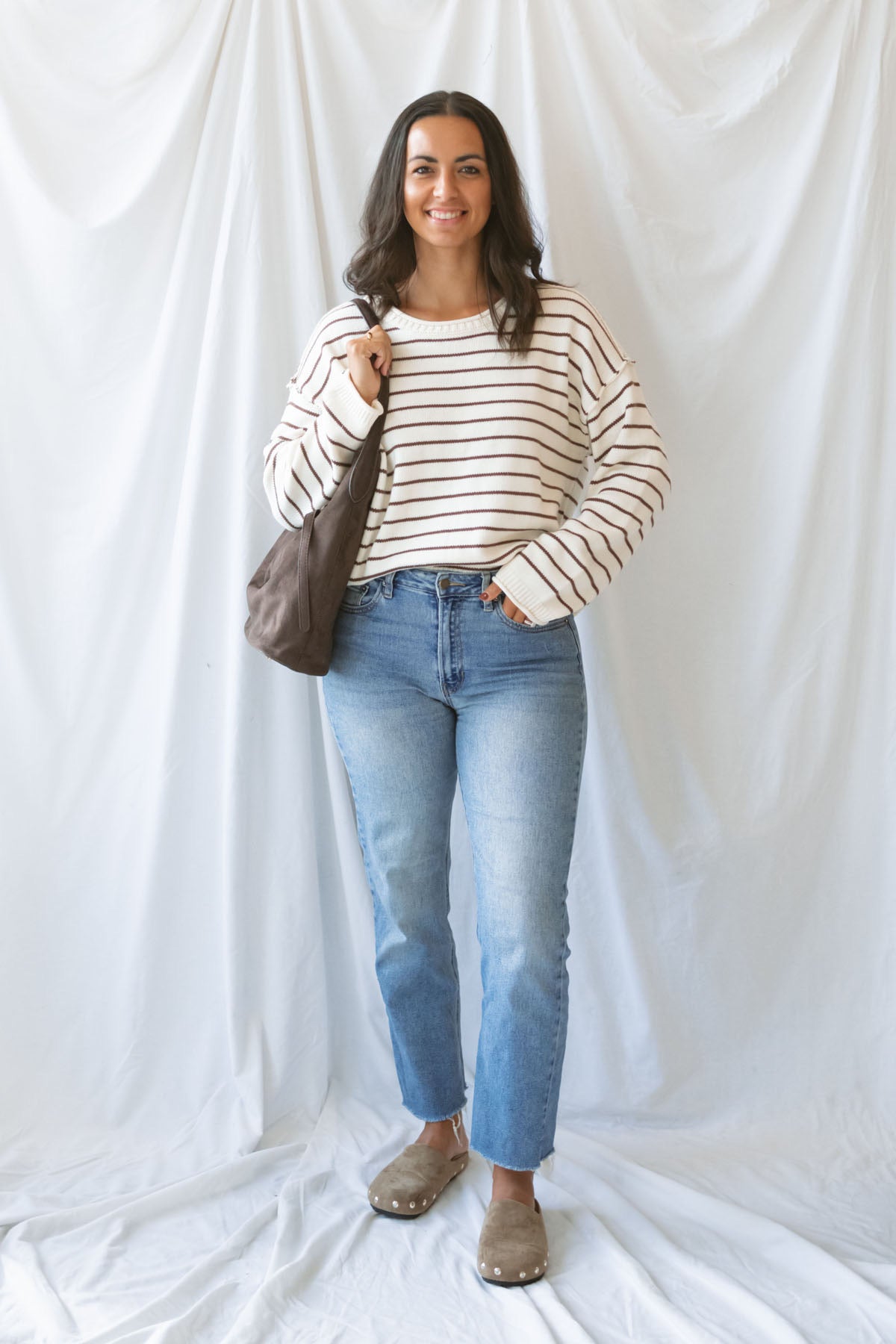 Model wearing striped crew neck sweater with raw edge detail. 