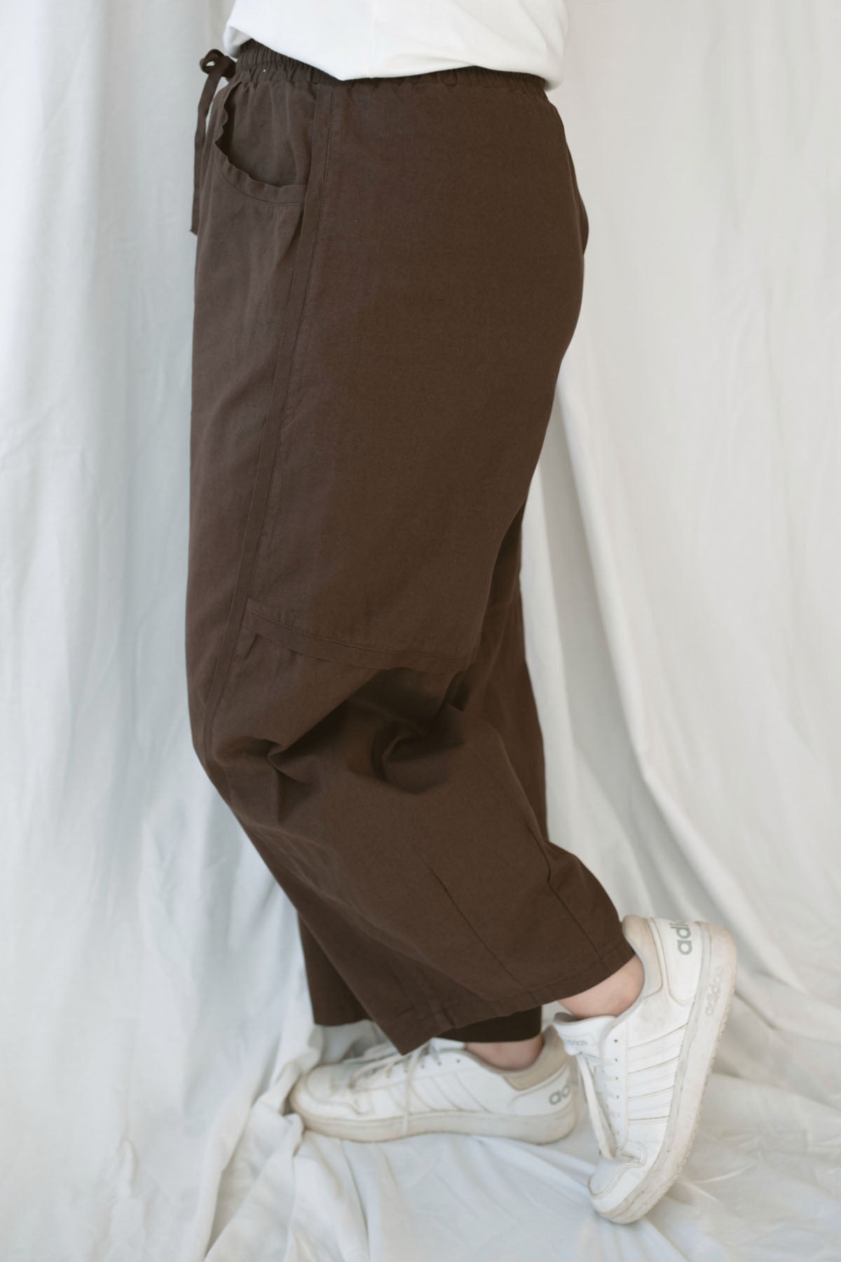 Model wearing the drawstring barrel style pant in coffee bean brown. 