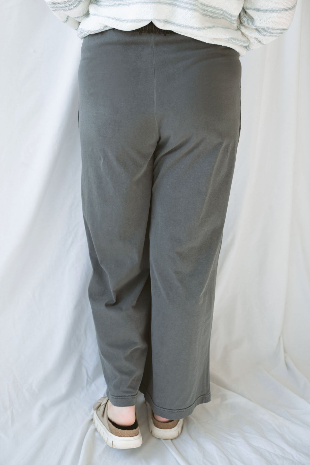 Back view of model wearing cotton wide leg pants with drawstring waistband. Model has the pants styled with a lightweight sweater, but they can be paired with other basics tees or blouses. 