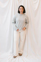 Model is wearing solid heather grey crew neck sweater. Styled with cream twist barrel pants. 