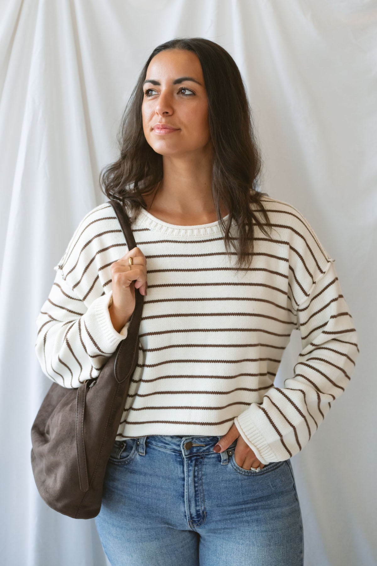 Model wearing striped crew neck sweater with raw edge detail. 