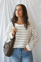 Model wearing striped crew neck sweater with raw edge detail. 