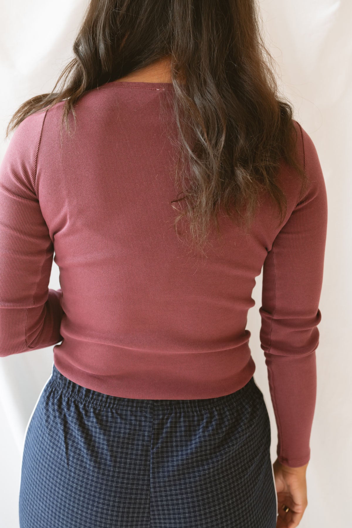 Back view of model wearing ribbed long sleeve top with boat style neckline. Model has top styled with our navy checkered wide leg pants, but could be paired with a variety of bottoms. 