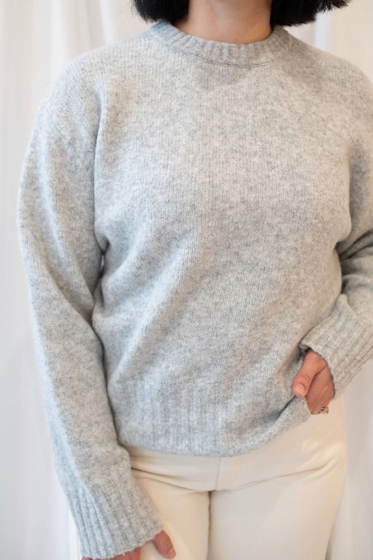 Model is wearing solid heather grey crew neck sweater. Styled with cream twist barrel pants. 