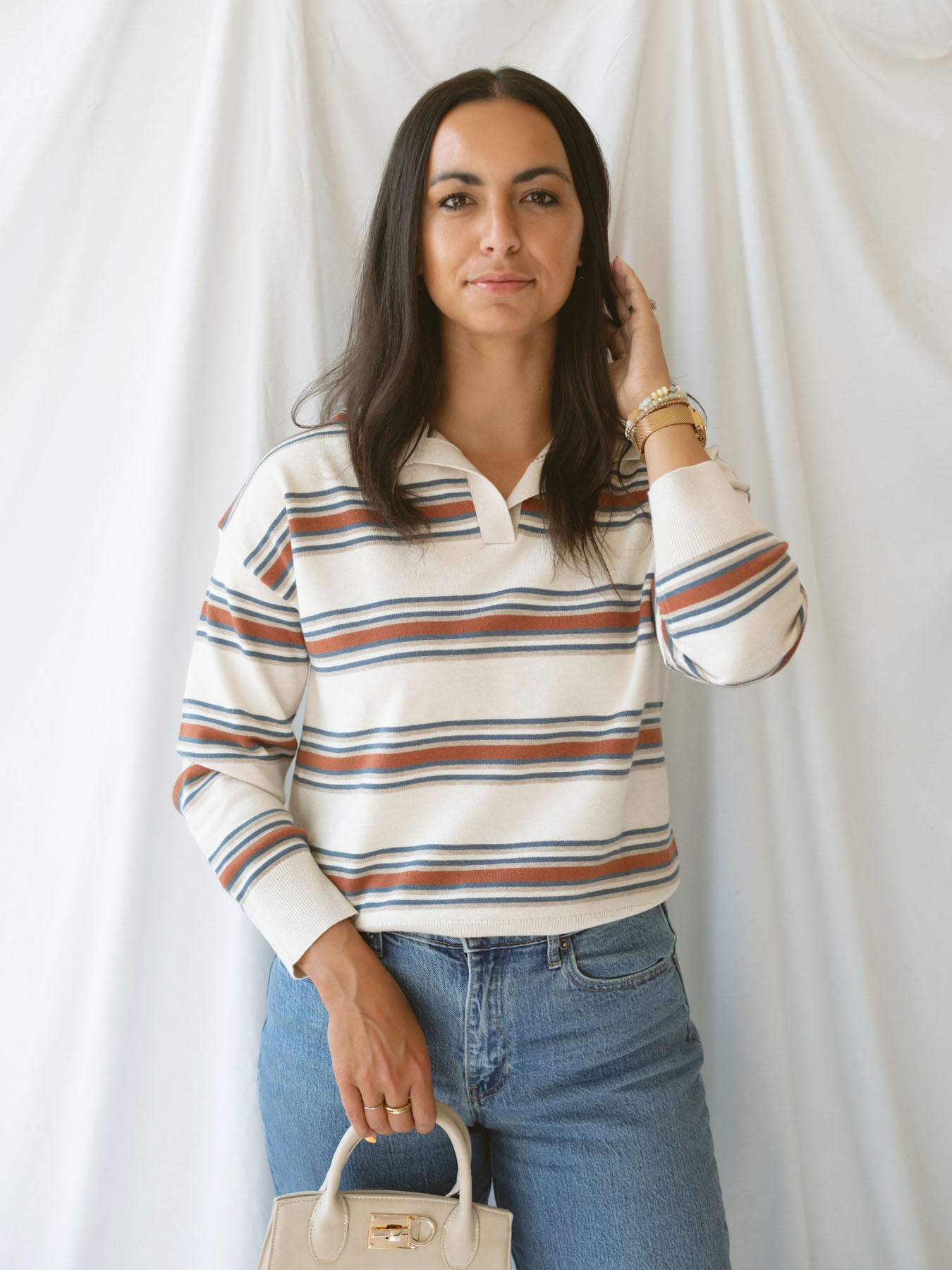 Model wearing the collared striped polo sweater. Off white, rust, and teal give this shirt a retro vibe while still bringing a modern twist. 