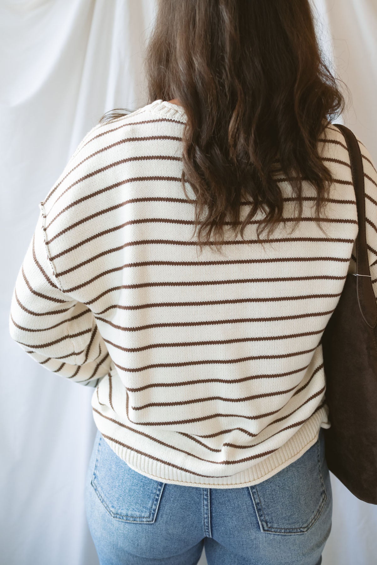 Model wearing striped crew neck sweater with raw edge detail. 