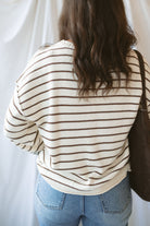 Model wearing striped crew neck sweater with raw edge detail. 