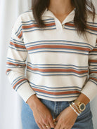 Model wearing the collared striped polo sweater. Off white, rust, and teal give this shirt a retro vibe while still bringing a modern twist. 