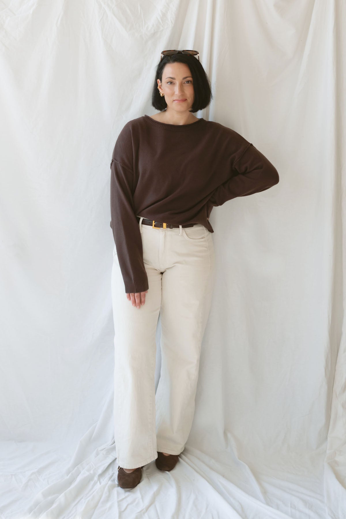 Model wearing the boat neck raw edge pullover sweater in espresso brown. Warm and cozy. Model paired the sweater with a cream pant and belt to give a more elevated look. 