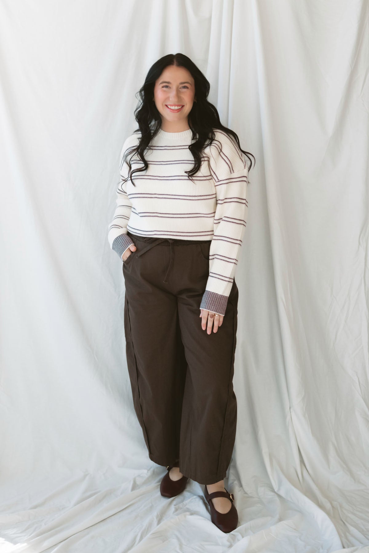 Model wearing a knit striped sweater in cream with burgundy. 
