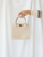 Model holding small nixie tote bag with top handle and metal fastened detail. 