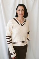 Charlotte cream cable knit V-neck varsity sweater with chocolate brown accents and classic collegiate-inspired details.