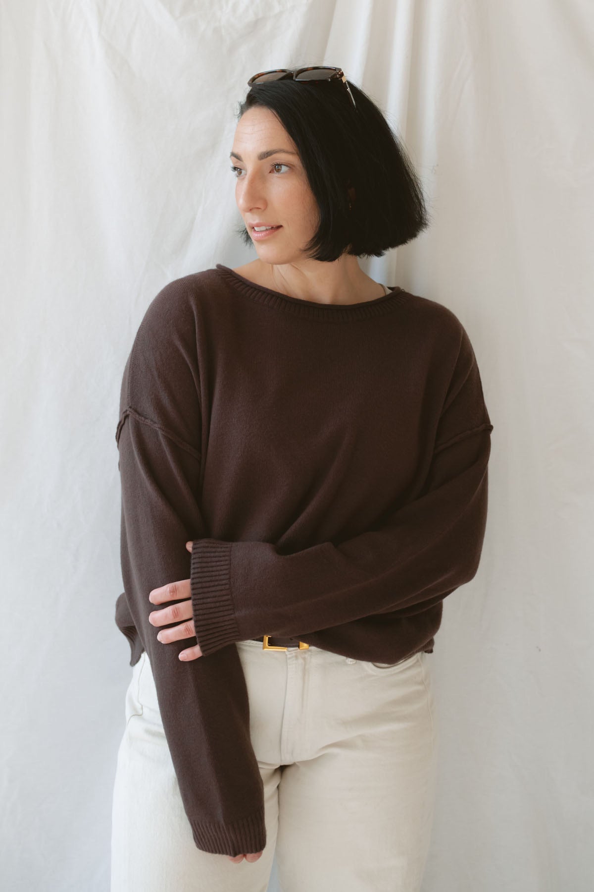 Model wearing the boat neck raw edge pullover sweater in espresso brown. Warm and cozy. Model paired the sweater with a cream pant and belt to give a more elevated look. 