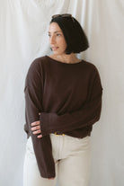 Model wearing the boat neck raw edge pullover sweater in espresso brown. Warm and cozy. Model paired the sweater with a cream pant and belt to give a more elevated look. 