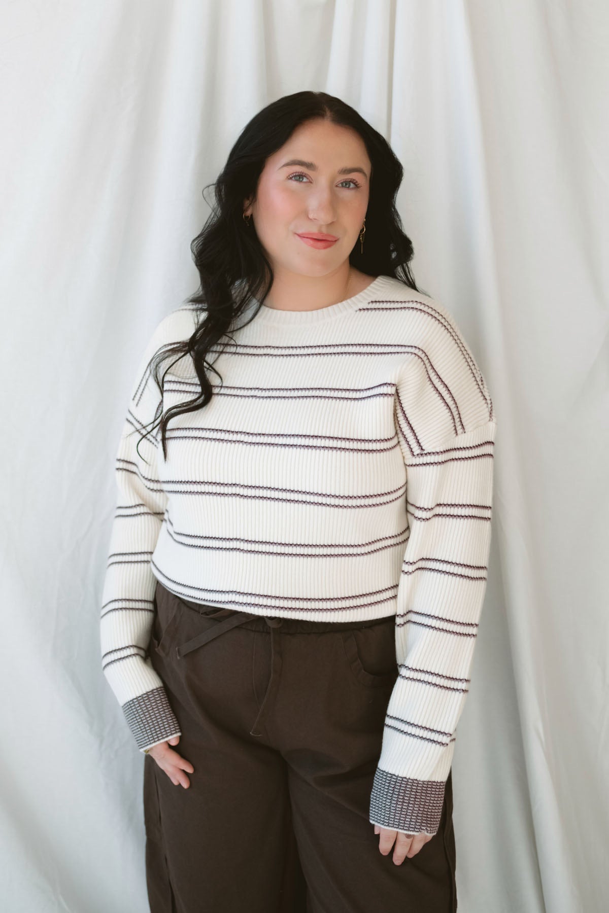 Model wearing a knit striped sweater in cream with burgundy. 
