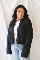 Model wearing the navy full button raw edge cardigan. Styled fully unbuttoned over a cream tank and paired with basic denim jeans. 