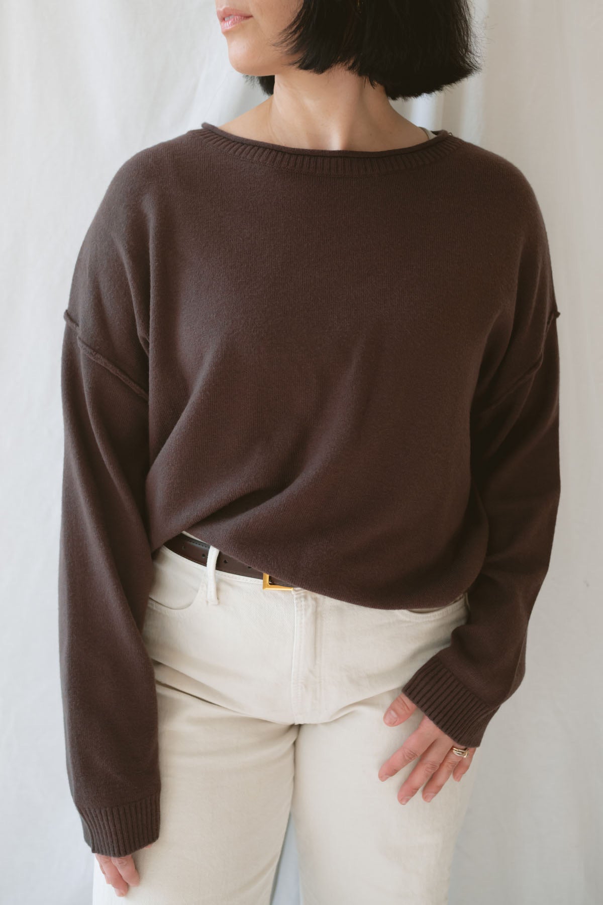 Model wearing the boat neck raw edge pullover sweater in espresso brown. Warm and cozy. Model paired the sweater with a cream pant and belt to give a more elevated look. 