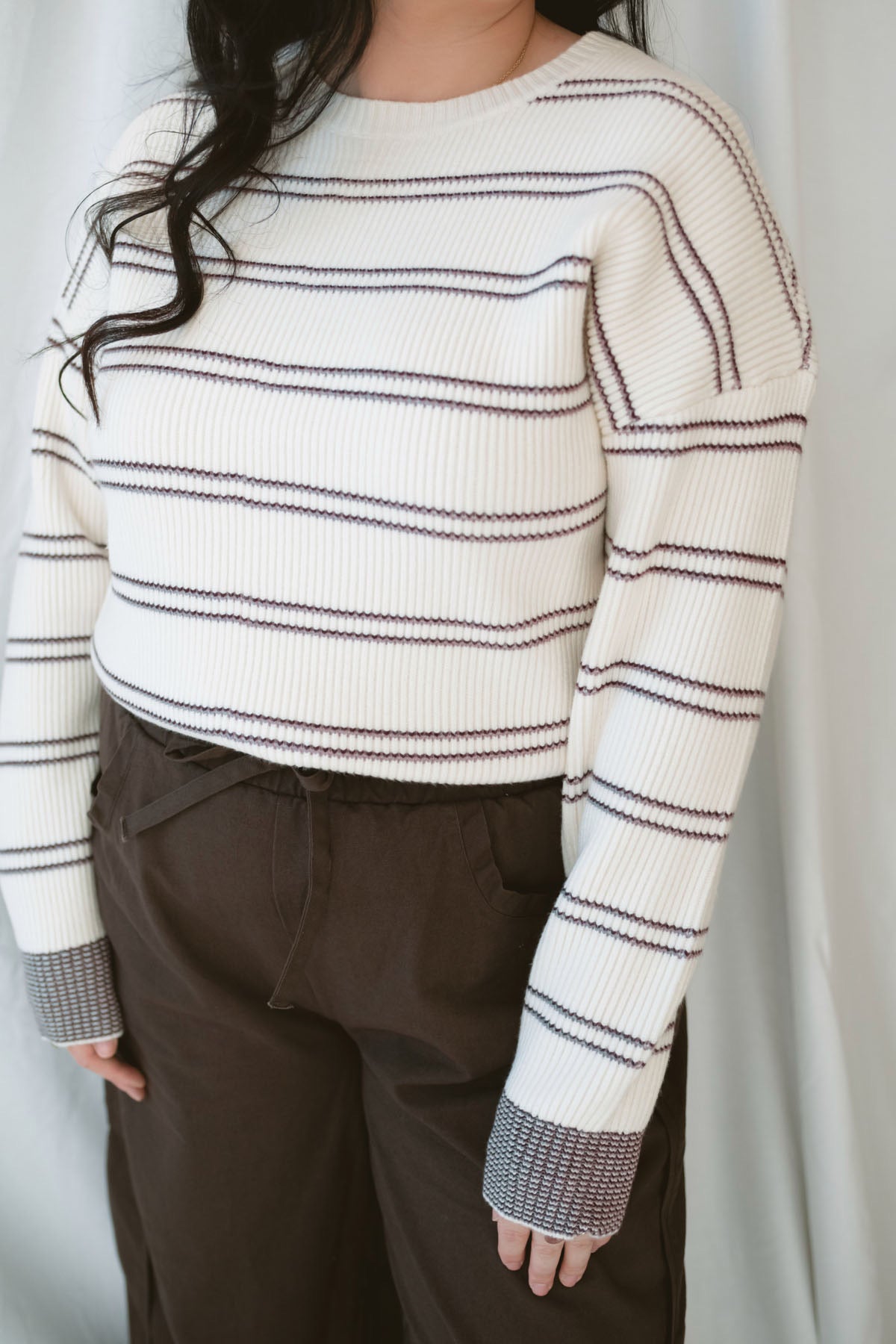 Model wearing a knit striped sweater in cream with burgundy. 