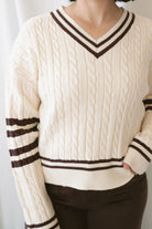 Charlotte cream cable knit V-neck varsity sweater with chocolate brown accents and classic collegiate-inspired details.